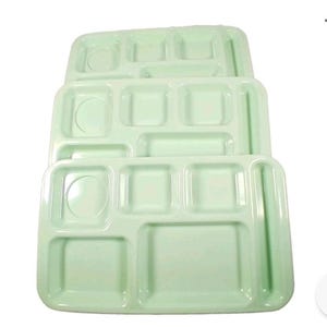 May include: A stack of three rectangular light mint green plastic cafeteria trays. Each tray features a molded design with one circular compartment, four square or rectangular food sections, and a long narrow slot for utensils.