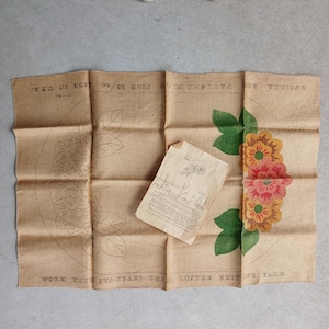 Könnte beinhalten: Ein Vintage-Bastelprojekt aus Jute mit floralem Design. Die entfaltete Jute hat ein gedrucktes Blumenmuster und Text, mit einem separaten Anleitungsblatt. Die Blumen sind in Orange-, Rosa- und Gelbtönen gehalten, mit grünen Blättern.