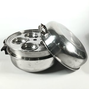 Pode incluir: Uma panela de vapor de aço inoxidável com a tampa ligeiramente entreaberta. A panela tem um design de vários níveis com um inserto perfurado para cozinhar alimentos no vapor. A tampa tem uma pega e é projetada para cozinhar vários pratos.