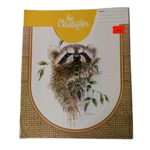 May include: A vintage "The Classifiler" file folder with a raccoon illustration. The cover has a yellow top section with the title, a beige border, and a woven texture. A red sticker is on the right side.