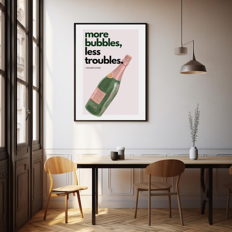 May include: A framed art print featuring a green champagne bottle illustration with pink accents. The artwork includes the text "more bubbles, less troubles" in green, with "CHAMPAGNE" below. The print is displayed in a dining room setting.