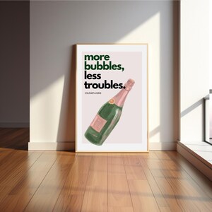 May include: A framed art print featuring a champagne bottle illustration. The bottle is green with a pink label and top. The print has the text "more bubbles, less troubles" in green, with "champagne" below.