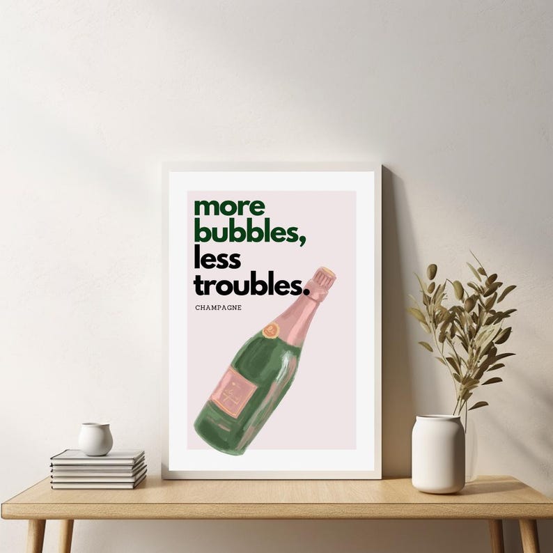 May include: A framed art print featuring a green champagne bottle with a pink label and top. The print has the text "more bubbles, less troubles." in green and black. The word "CHAMPAGNE" is below the text.