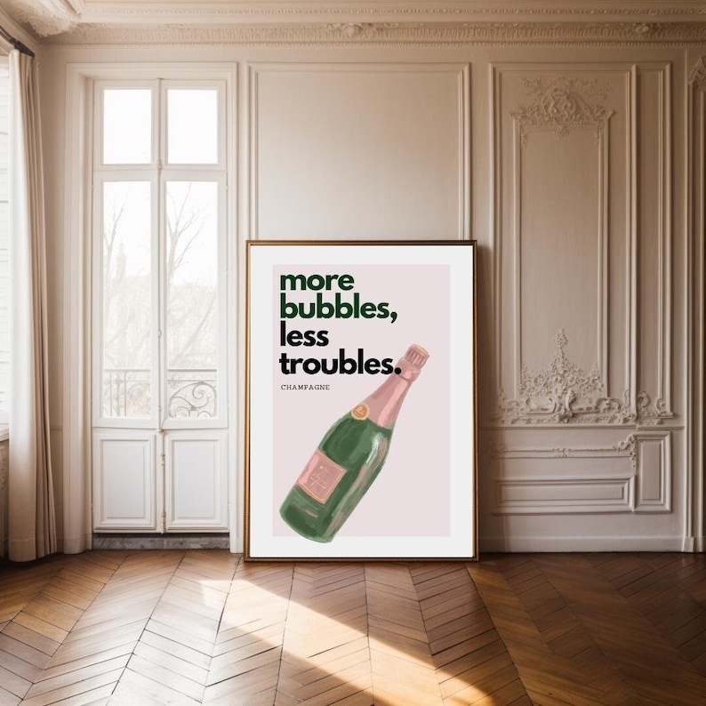 May include: A framed art print featuring a champagne bottle illustration. The artwork has a light pink background with the text "more bubbles, less troubles." The champagne bottle is green and pink, with the word "CHAMPAGNE" below the text.