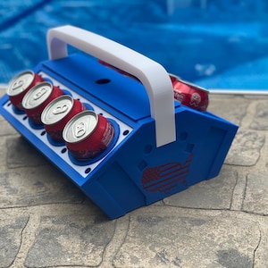 Può includere: Frigorifero blu e bianco con maniglia e design della bandiera americana. Il frigorifero è pieno di lattine rosse e bianche.