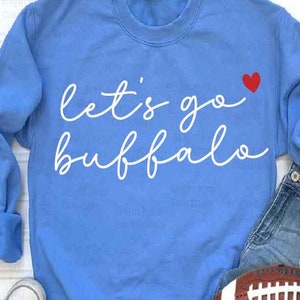 May include: A light blue sweatshirt with the text "Let's go Buffalo" in white cursive lettering and a small red heart.
