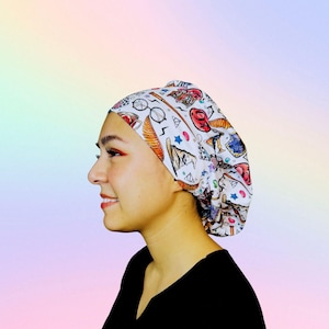 May include: A white cap with a colorful pattern featuring various illustrations. The cap is adorned with images of glasses, stars, and other whimsical designs. The cap is worn by a person wearing a black shirt.