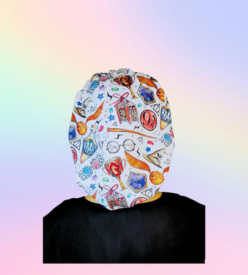 May include: White patterned cap featuring various Harry Potter-themed illustrations, including a golden snitch, potion bottles, and the Hogwarts crest. The cap is worn over a black shirt.