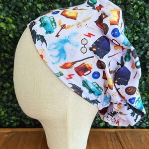 May include: White fabric head covering with a repeating pattern of fantasy-themed illustrations. The design includes images of a blue car, a golden key, a broom, and a pair of glasses. The head covering is displayed on a mannequin head.