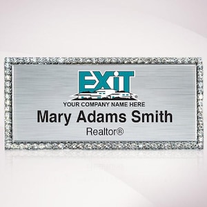 May include: Silver name tag with a diamond-like border. The tag features the EXIT Realty logo and the text "YOUR COMPANY NAME HERE". Below the logo is the name "Mary Adams Smith" and the title "Realtor®".
