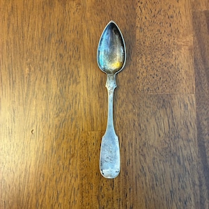 May include: A white ceramic mug with a black handle and the text "But First, Coffee" in a black, bold font. The mug is sitting on a white surface. The mug is approximately 4 inches tall.