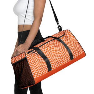Könnte beinhalten: Orange-weiße karierte Reisetasche mit schwarzen Trägern und einer Netztasche. Die Tasche hat ein wirbelndes Karomuster.