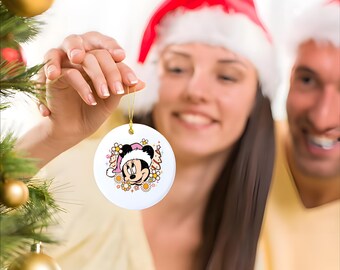 May include: A white ceramic Christmas ornament with a colorful image of Minnie Mouse wearing a Santa hat and surrounded by flowers.