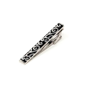 May include: A silver tie clip with a black, intricate, scroll-like design.