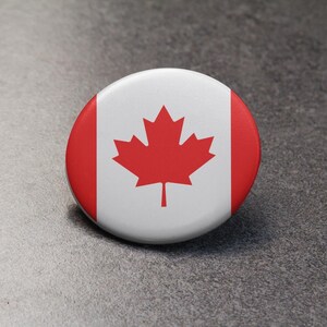 May include: A round button featuring the Canadian flag. The flag is red and white with a red maple leaf in the centre.