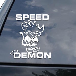 May include: White decal featuring the word "SPEED" above a cartoon demon character and the word "DEMON" below. The decal is on a black car window. A diamond logo is visible in the lower right corner.