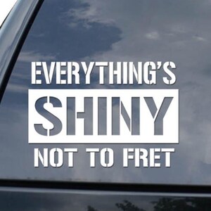May include: White vinyl decal applied to a black vehicle window. The decal reads "EVERYTHING'S SHINY NOT TO FRET" in a bold, blocky font. A diamond-shaped logo is visible in the lower right corner.