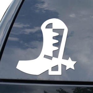 May include: White vinyl decal of a cowboy boot with a star spur. The decal is affixed to the rear window of a black vehicle. The boot design is a simple, stylized outline.