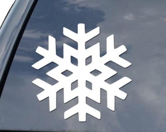 May include: A white snowflake decal is affixed to the rear window of a black vehicle. The snowflake design is intricate and symmetrical, with six points. The decal is positioned on the left side of the window, with a logo visible on the right.