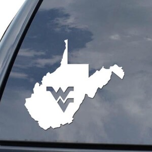 May include: White vinyl decal of the state of West Virginia with the WVU logo, applied to a vehicle's rear window. The decal is a simple outline of the state's shape, with the logo in the lower left corner. The background shows a cloudy sky.