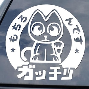 May include: White vinyl car decal featuring a cartoon cat with large eyes and a raised paw, surrounded by Japanese text. The cat is inside a white circle with additional Japanese text and stars. The decal is applied to a black car window.