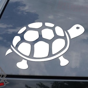 May include: White turtle decal applied to a car window. The turtle design is a simple outline, featuring a segmented shell, head, and four legs. The decal is positioned on the rear window of a black vehicle, with a cloudy sky visible through the glass.