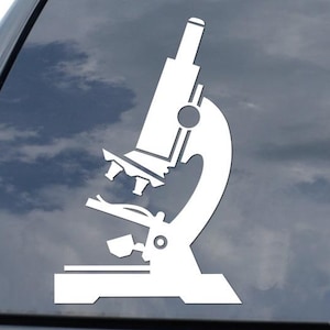 May include: White vinyl decal of a microscope, affixed to the rear window of a black vehicle. The microscope is a simplified, stylized illustration, featuring the essential components of a laboratory microscope. The background shows a cloudy sky.
