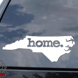 May include: White vinyl decal of the state of North Carolina with the word "home."  The decal is on the back window of a black car.