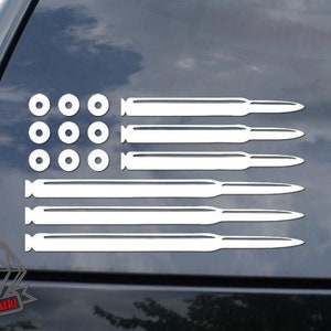 May include: A white vinyl decal of an American flag made of bullet casings. The flag has 13 stripes and 50 stars. The decal is on the back window of a car.