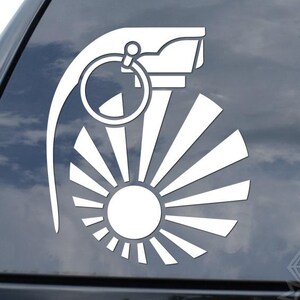 May include: White vinyl decal of a stylized grenade with a sunburst design. The design features a circular element with a pull ring and a sun with radiating lines, suitable for car windows or other surfaces.