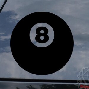 May include: Black vinyl decal of an eight ball, a classic symbol from the game of pool. The number 8 is in white, centered on a solid black circle. The decal is shown on a car window.