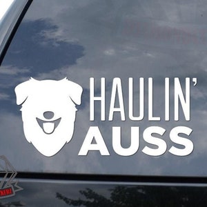 May include: White vinyl decal sticker for a car window. The sticker features a white silhouette of an Australian Shepherd dog's head with the text "HAULIN' AUSS" below it.