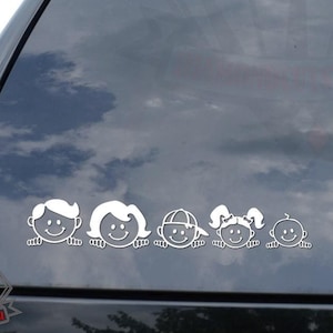 May include: White vinyl decal of a family of five peeking over a surface. The family includes two parents, two children, and a baby. The decal is on the back window of a black car.