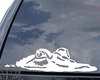 May include: White vinyl decal of an alligator's head peeking out of the water. The decal is applied to the rear window of a black SUV.
