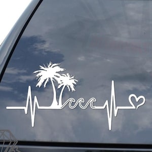 May include: White vinyl decal of a palm tree with a heart beat line and waves. The decal is on the back window of a black car.