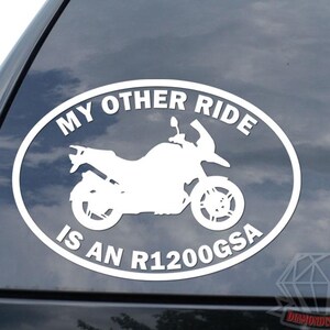 May include: White oval sticker with the text "MY OTHER RIDE IS AN R1200GSA" and a motorcycle silhouette. The sticker is on a dark surface, likely a car window. The design is simple and bold.