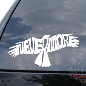 May include: White vinyl decal featuring the word "NEVERMORE" in a stylized font, shaped like a bird in flight. The decal is applied to the rear window of a black vehicle, with a cloudy sky visible through the glass.