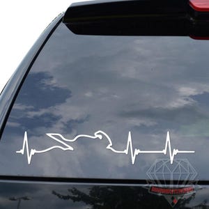 May include: White vinyl decal of a motorcycle integrated into a heartbeat line, applied to a car window. The design features a motorcycle silhouette within the rhythmic pattern, symbolizing a passion for motorcycles. The decal is a simple, yet striking, graphic.