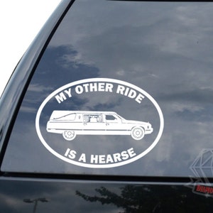 May include: White vinyl sticker with a black outline of a hearse and the text "My Other Ride Is A Hearse".