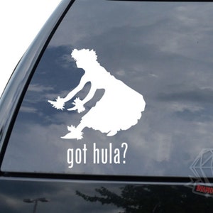 May include: White vinyl decal of a hula dancer in motion, with a floral headdress and leis. The text "got hula?" is below the dancer. The decal is designed for application on a car window or similar surface.