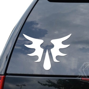 May include: White vinyl decal of a stylized angel wing design with a teardrop shape in the center. The decal is applied to the rear window of a black car.