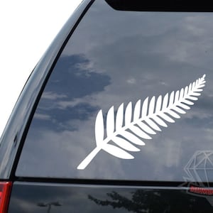 May include: White vinyl sticker of a silver fern, a symbol of New Zealand, on a car window.