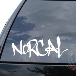 May include: White vinyl decal sticker with the word "NORCAL" written in a graffiti style font. The sticker is applied to the rear window of a black car.