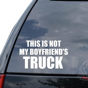 May include: White vinyl sticker with the text "This is not my boyfriend's truck" on a black car window.