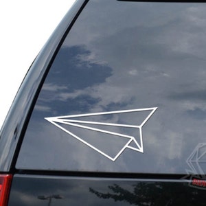 May include: White paper airplane outline decal for a car window. The decal is on a dark gray car window.