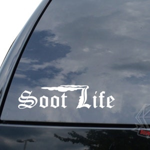May include: White vinyl decal with the text "Soot Life" in a stylized font. The text is accompanied by a graphic of a stylized smoke plume.