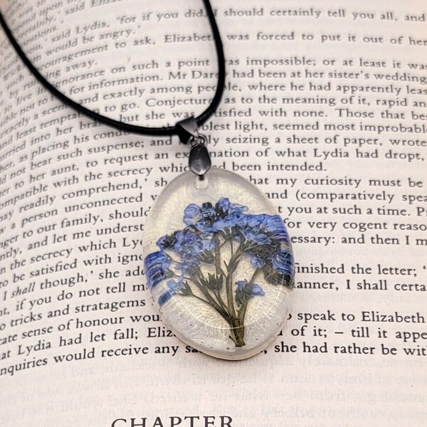 Blue forget-me-not flowers in a handmade resin oval pendant necklace with a glistening cream background