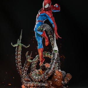 Op de afbeelding: Een rood en blauw Spider-Man-actiefiguur is geposeerd in een dynamische vechtpose, met een opgeheven been en een uitgestrekte arm. De figuur staat op een groot, meerarmige, mechanisch wezen met een bruine, rotsachtige basis.
