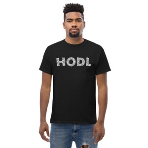 Puede incluir: Una camiseta negra con la palabra "HODL" impresa en blanco. Las letras están formadas por pequeños círculos blancos.