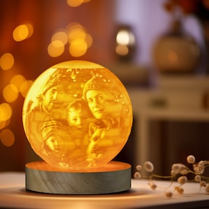 May include: A 3D printed glass globe night light with a warm glow, featuring a family portrait of four people. The globe is on a wooden base.